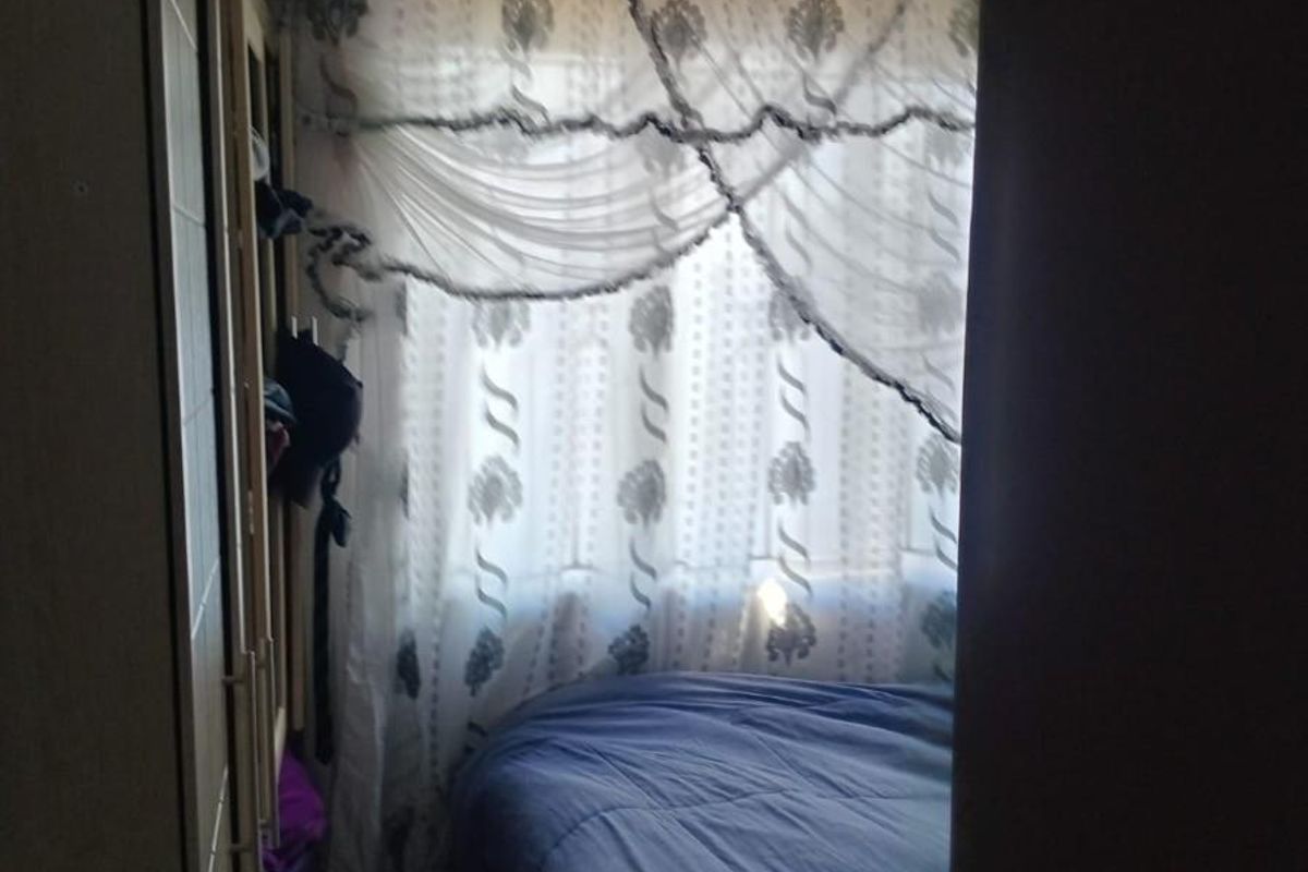 A bedroom featuring built-in cabinetry and a window with decorative curtains, viewed from the doorway.
