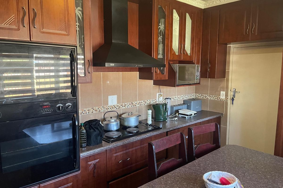 A functional kitchen featuring dark wood cabinetry, a built-in oven, a black extractor fan, and a tiled backsplash with a decorative mosaic border.