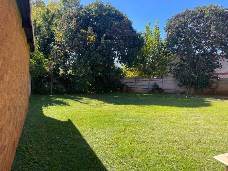 A spacious rear garden featuring a well-maintained lawn, mature trees, and a solid boundary wall, offering a private outdoor space.