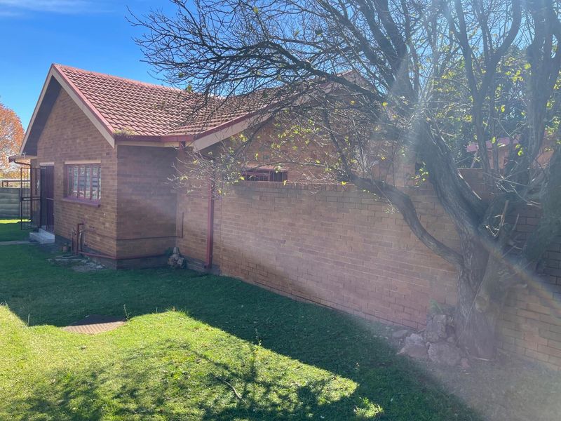 A view of the exterior rear of the brick house, featuring a tiled roof, perimeter boundary wall, and a small garden area.