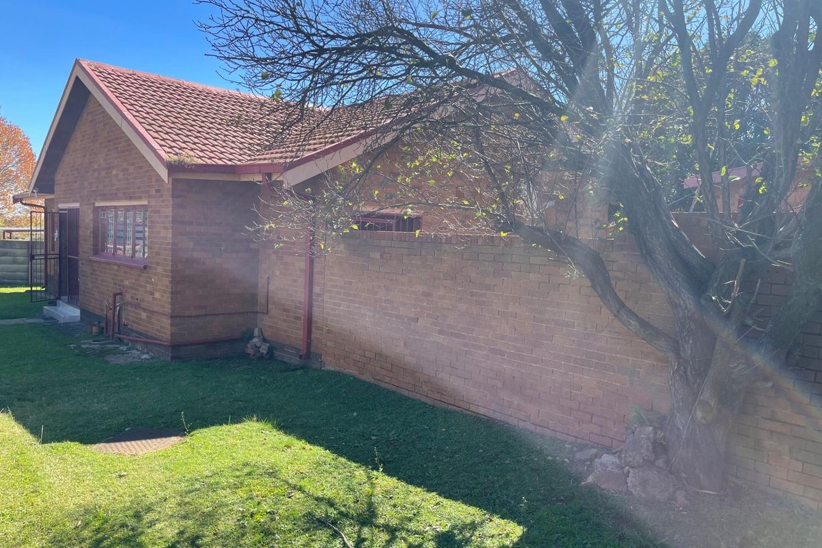 A view of the exterior rear of the brick house, featuring a tiled roof, perimeter boundary wall, and a small garden area.