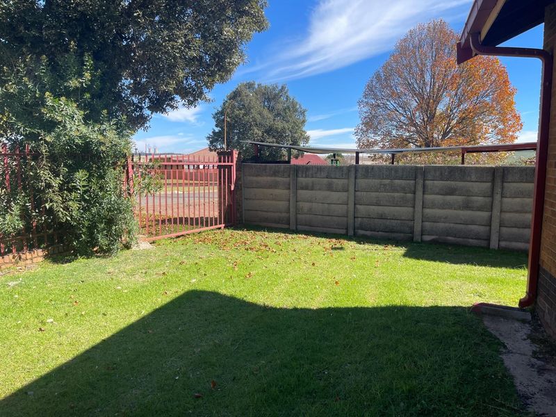 A private rear garden area featuring a lawn, enclosed by a precast concrete boundary wall and a metal security gate.