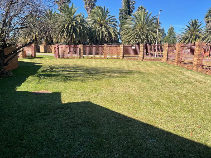 A spacious, well-maintained garden area featuring a manicured lawn, enclosed by a secure brick and metal perimeter fence with integrated gate access.