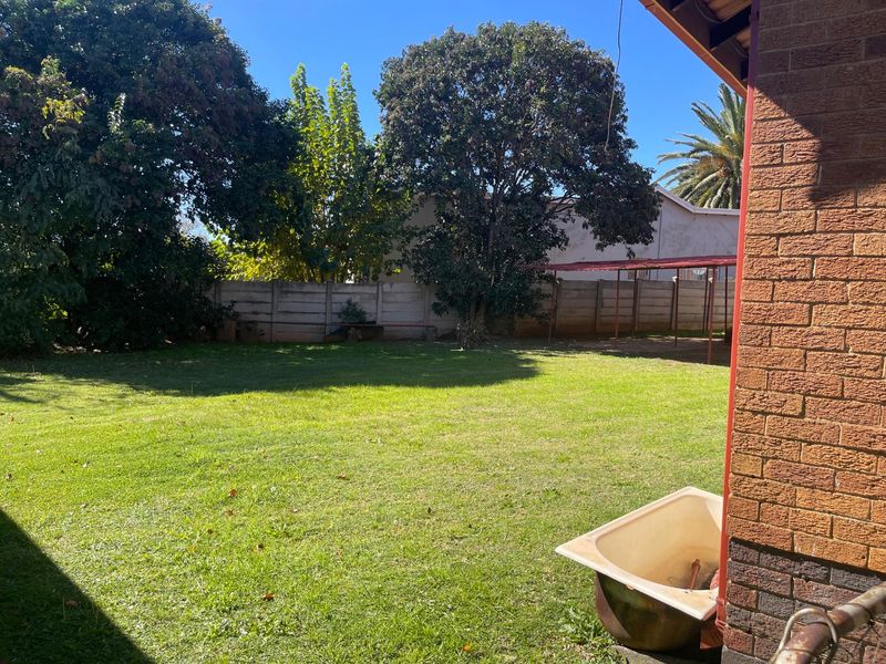 A spacious rear garden featuring a large lawn area, mature trees, and a perimeter boundary wall.