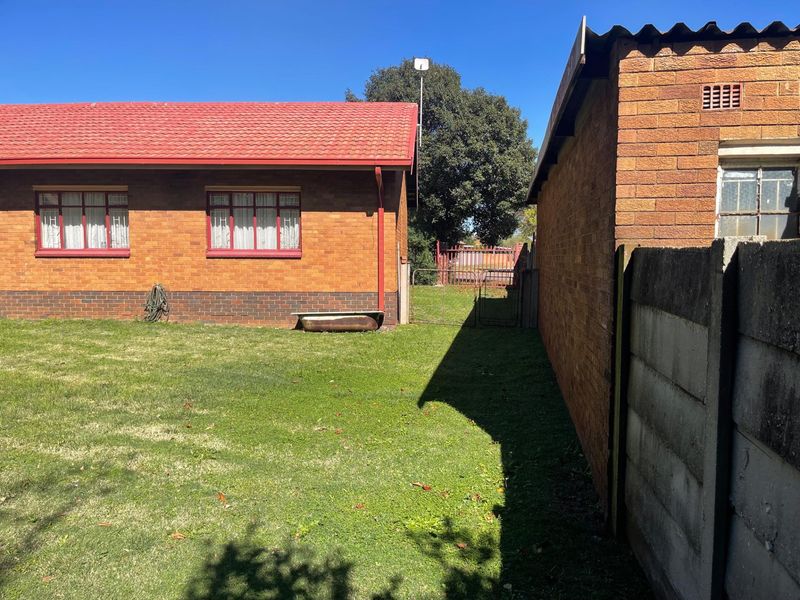 A view of the side garden area featuring a brick exterior, tiled roof, and perimeter boundary wall.