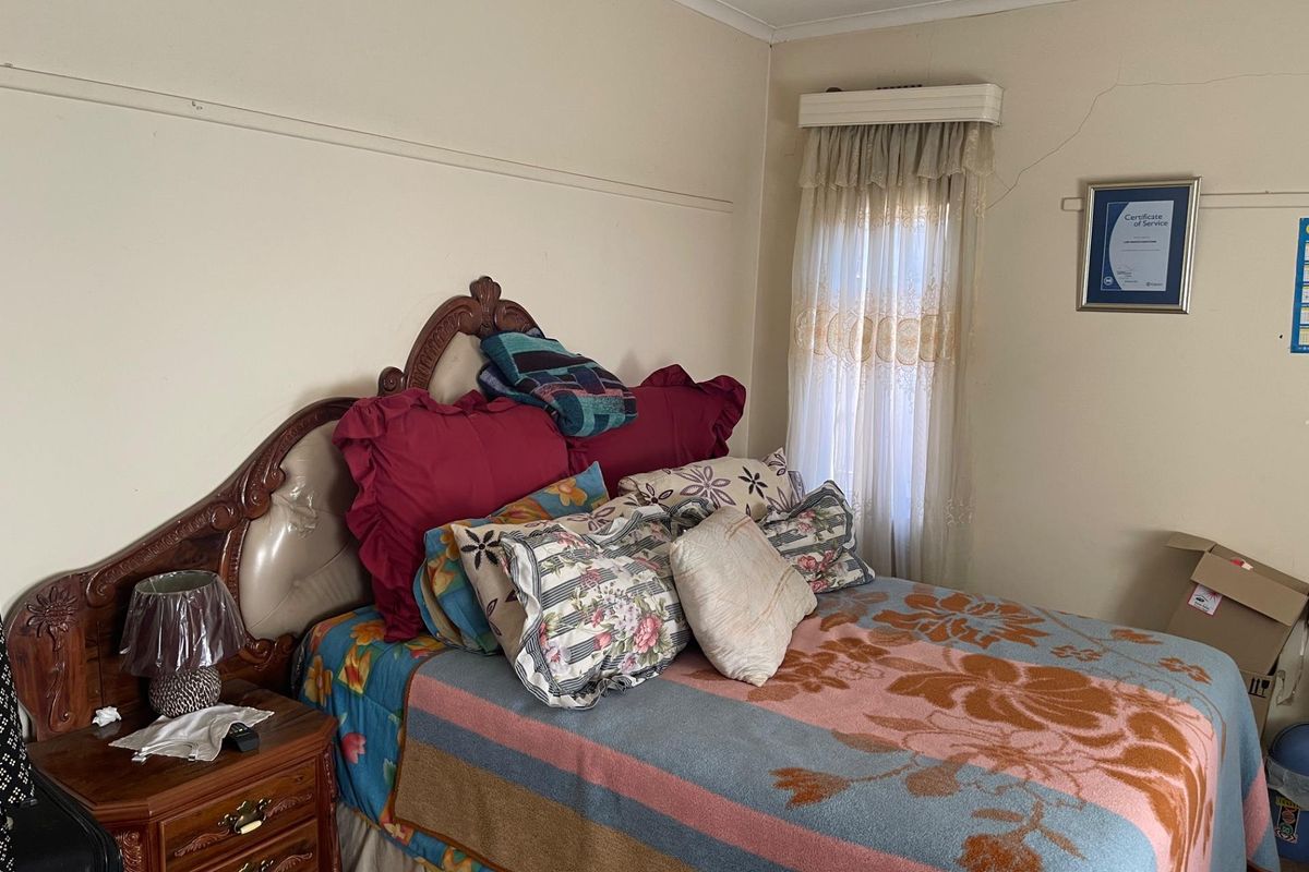 A bedroom featuring a window with fitted curtain rail and visible wall cracking requiring maintenance.