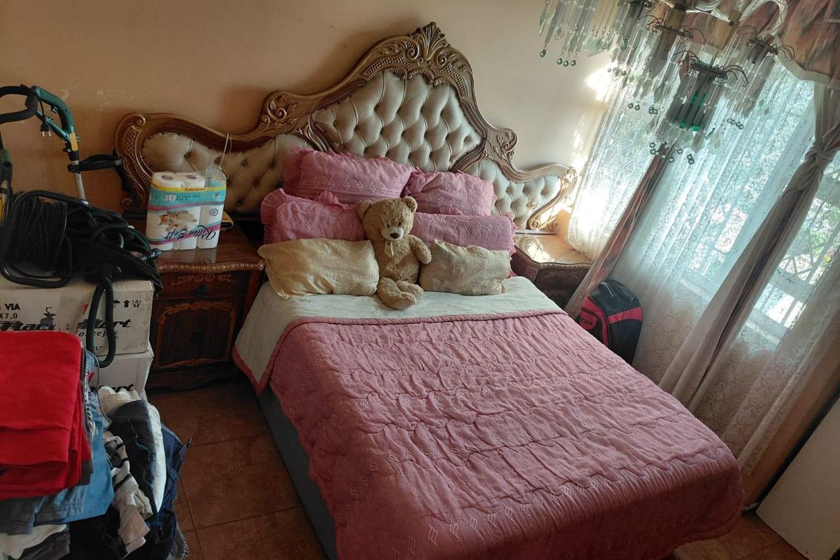 A bedroom featuring a large ornate headboard, tiled flooring, and a decorative crystal chandelier, offering a traditional aesthetic.