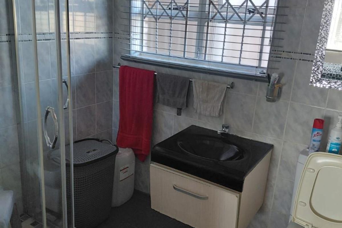 A functional bathroom featuring a glass-enclosed shower, a wall-mounted vanity with a basin, and a toilet, finished with tiled walls and flooring.
