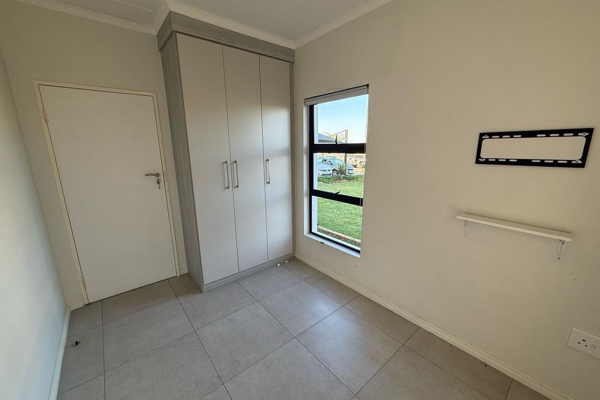 A clean, empty bedroom featuring neutral tiled flooring, a modern built-in wardrobe, and a window providing natural light.