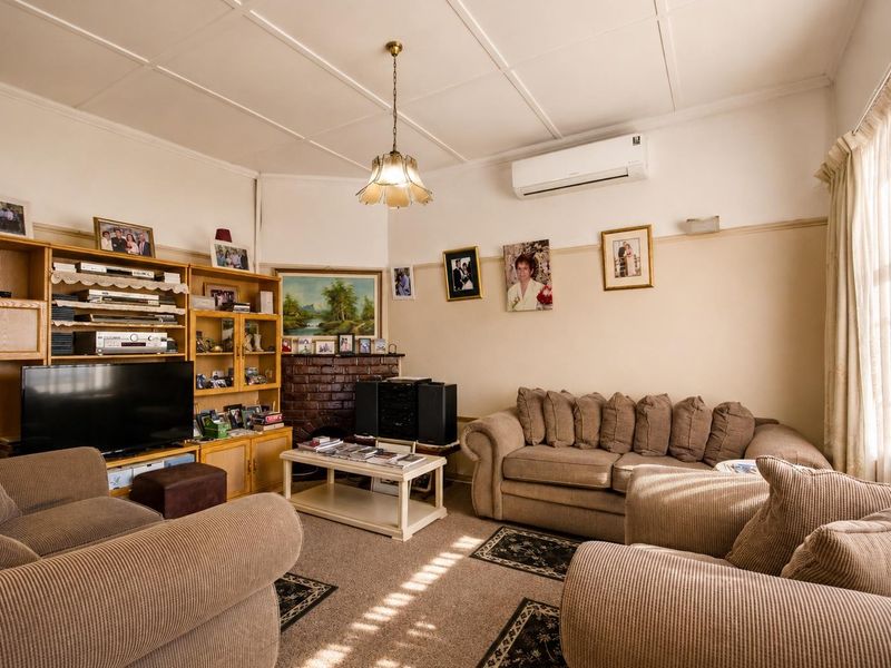 A comfortable living room featuring a classic brick fireplace, split-system air conditioning, and traditional panelled ceiling details.