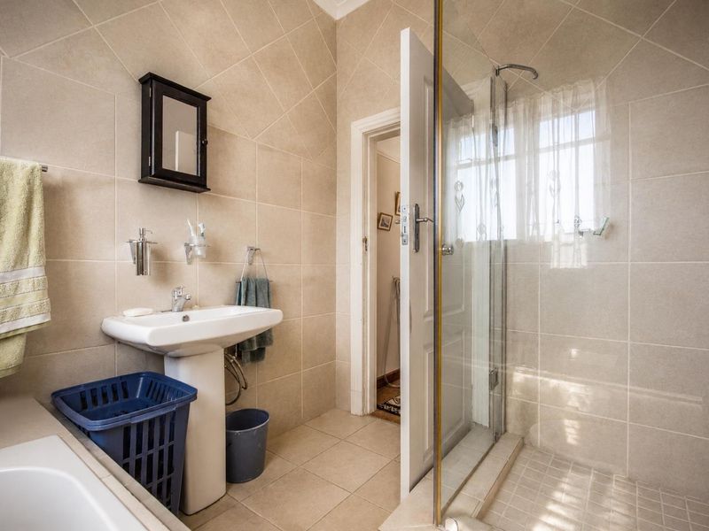 A functional bathroom featuring a pedestal washbasin, a glass-enclosed shower, and neutral wall and floor tiling.