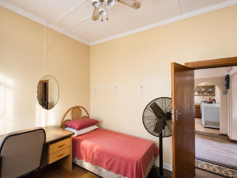 A bedroom featuring high ceilings with a decorative rose, timber door, and access to the adjacent kitchen area.