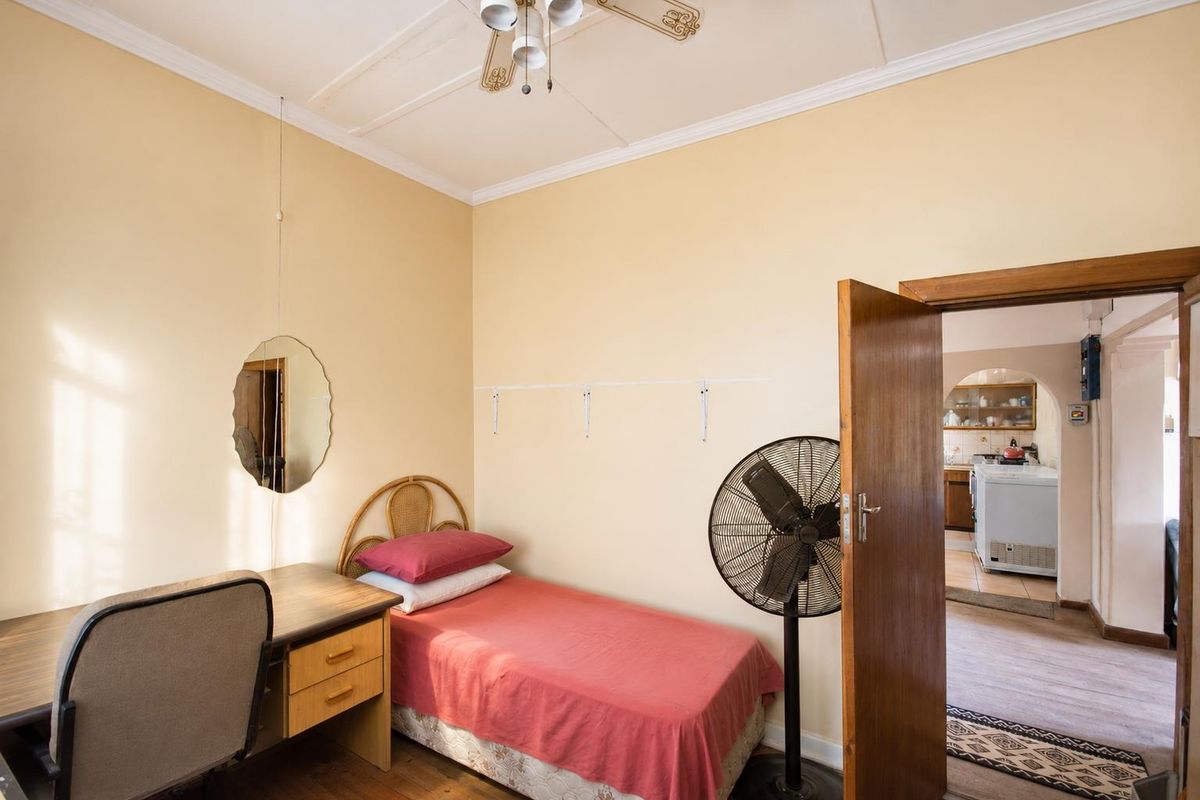 A bedroom featuring high ceilings with a decorative rose, timber door, and access to the adjacent kitchen area.