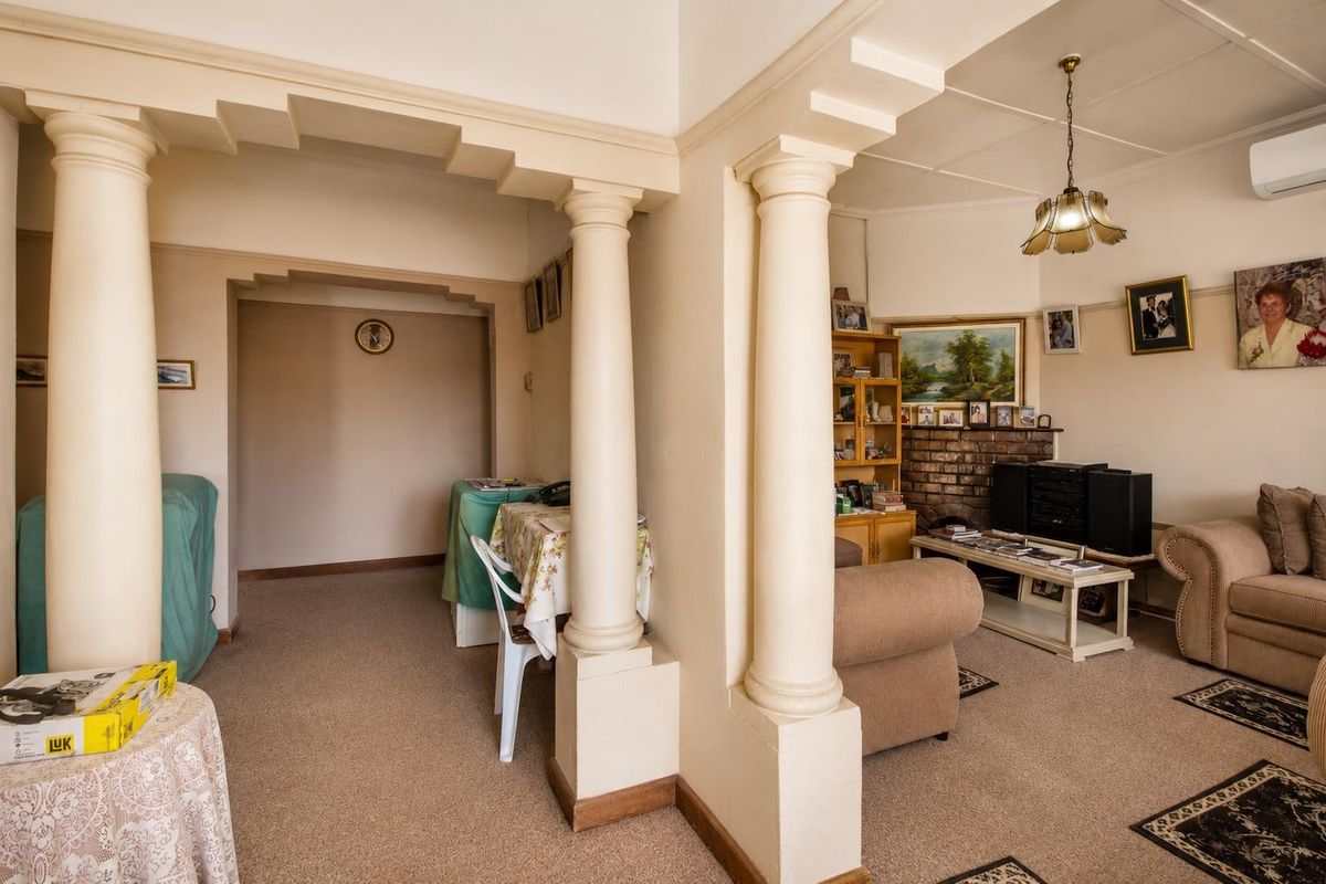 A living room featuring decorative columns, a brick fireplace, and a split-system air conditioner, offering a traditional layout with connected living and dining spaces.