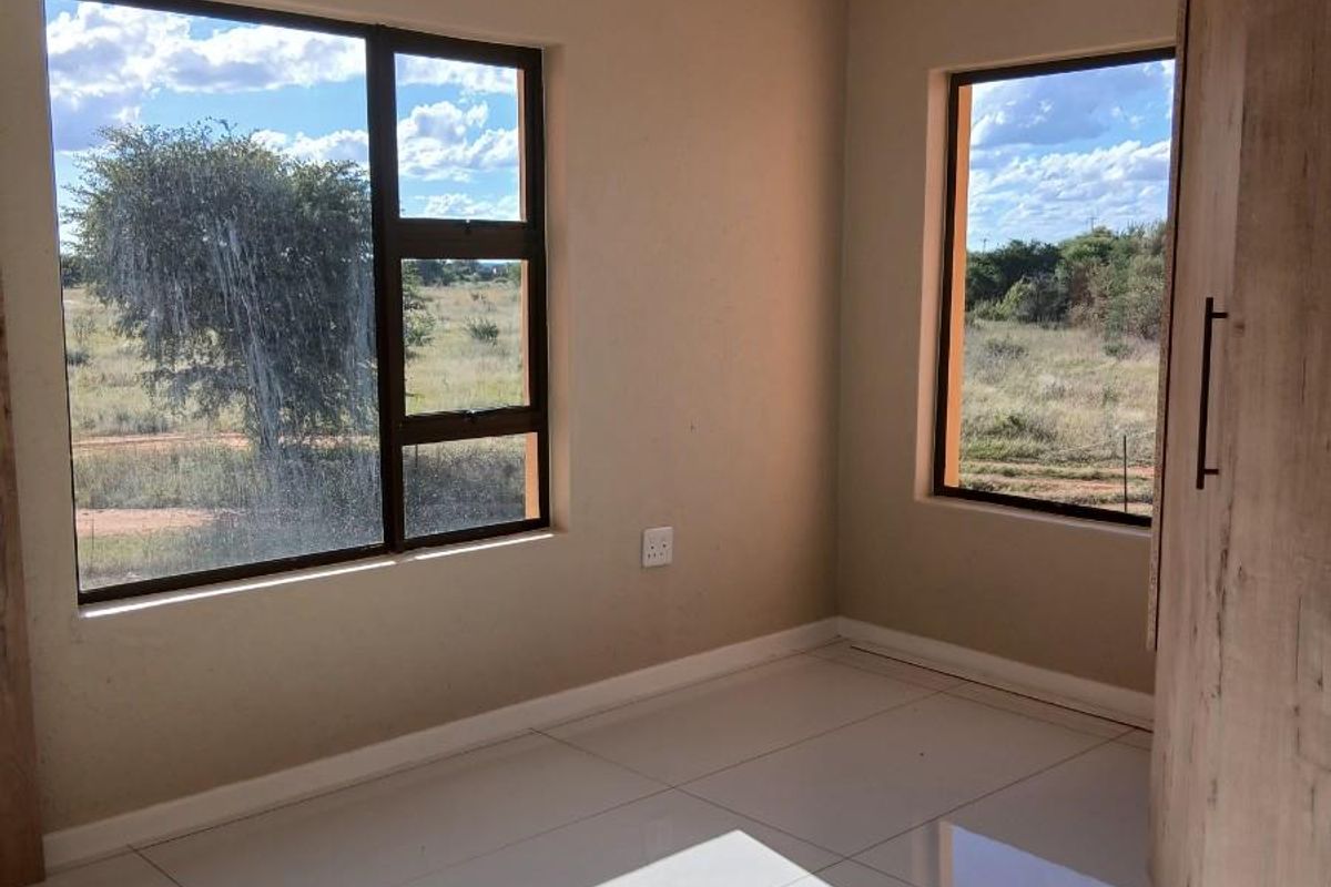 A bright, empty bedroom featuring large windows with natural views, tiled flooring, and built-in wooden cabinetry.