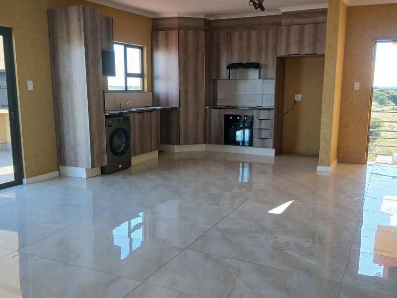 Open plan kitchen and living area featuring modern wood-look cabinetry, built-in oven, hob, extractor fan, and polished porcelain floor tiles.