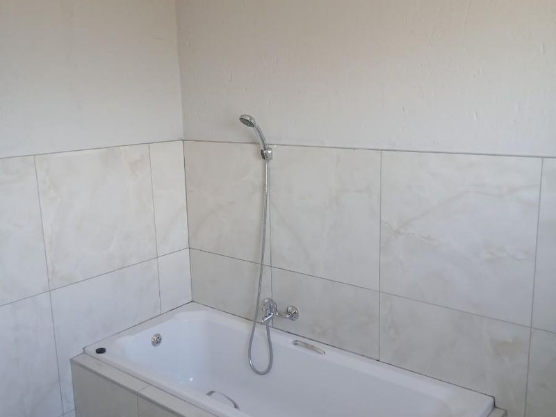 A clean bathroom featuring a built-in bathtub with a handheld shower fixture and neutral wall tiling.