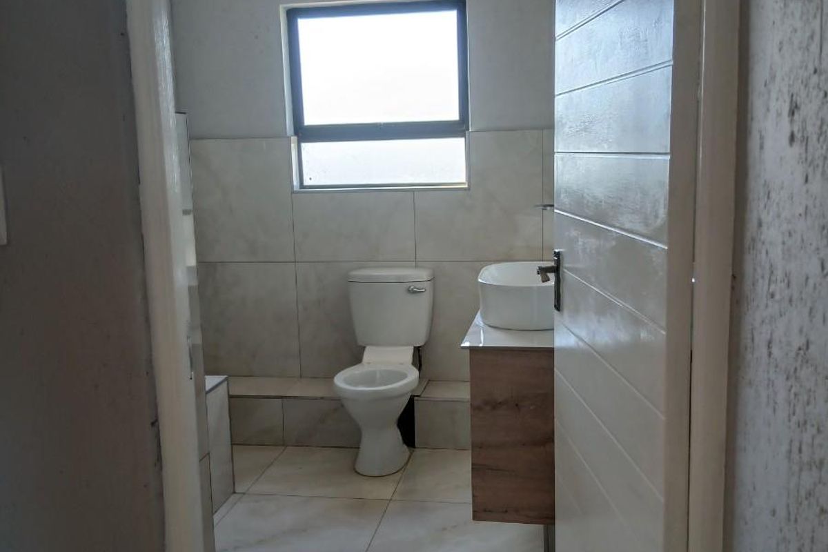 A modern bathroom featuring a wall-mounted vanity with a vessel sink, a standard toilet, and neutral floor-to-ceiling tiling.