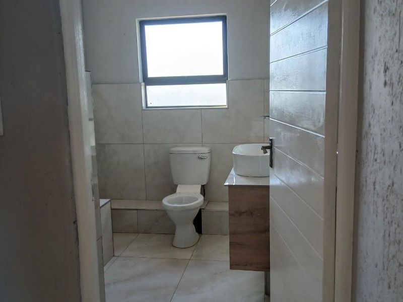 A modern bathroom featuring a wall-mounted vanity with a vessel sink, a standard toilet, and neutral floor-to-ceiling tiling.