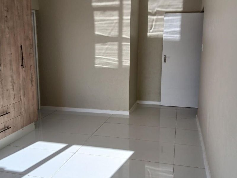 A bright, empty bedroom featuring neutral wall tones, polished porcelain floor tiles, and built-in wooden cabinetry.