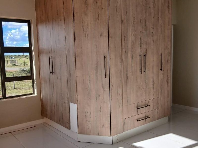 A bright bedroom featuring large format floor tiles and a substantial, modern wood-grain built-in wardrobe unit.