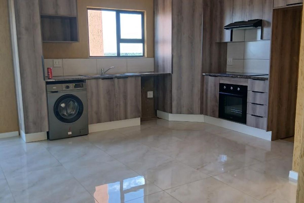 Modern kitchen featuring wood-grain cabinetry, built-in oven, extractor fan, tiled flooring, and integrated space for a washing machine.