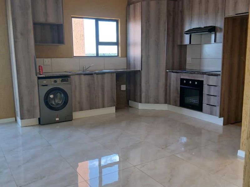 Modern kitchen featuring wood-grain cabinetry, built-in oven, extractor fan, tiled flooring, and integrated space for a washing machine.