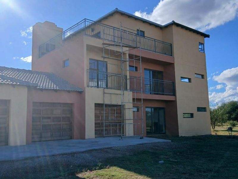 Rear view of a multi-story apartment building featuring balconies, sliding glass doors, and integrated garage doors, currently undergoing exterior maintenance.