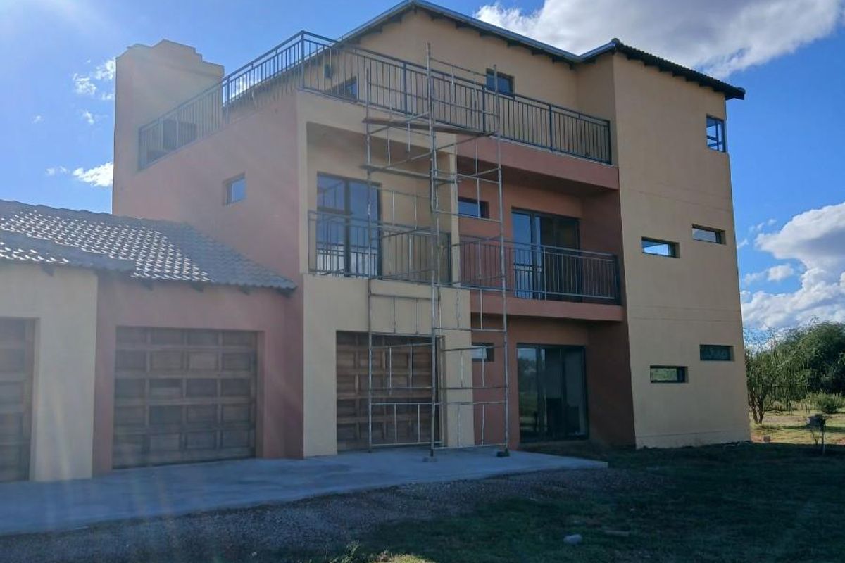 Rear view of a multi-story apartment building featuring balconies, sliding glass doors, and integrated garage doors, currently undergoing exterior maintenance.