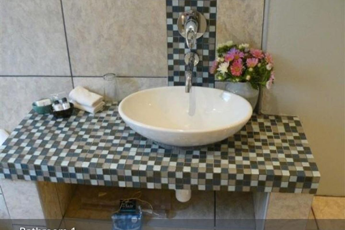 A bathroom vanity featuring a vessel sink mounted on a tiled countertop with mosaic detailing and wall-mounted chrome faucet fixtures.
