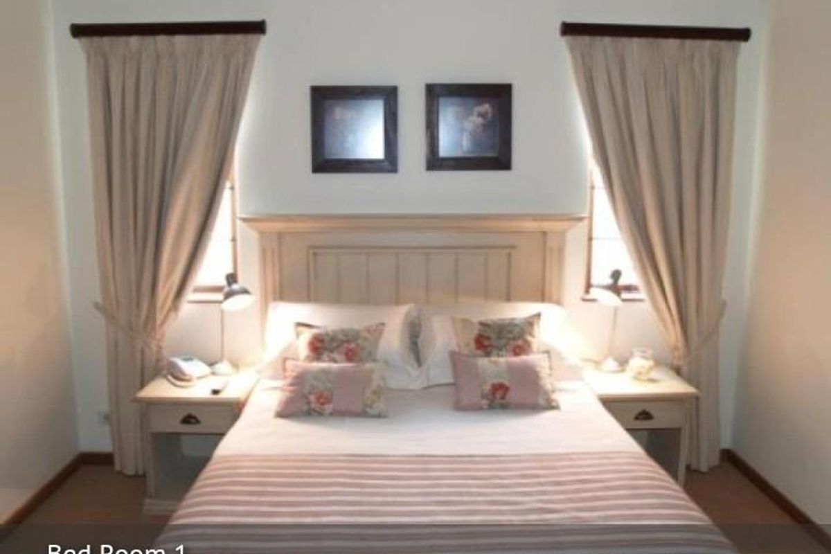 A well-maintained bedroom featuring a built-in headboard, dual windows with curtain rods, and integrated bedside cabinetry.