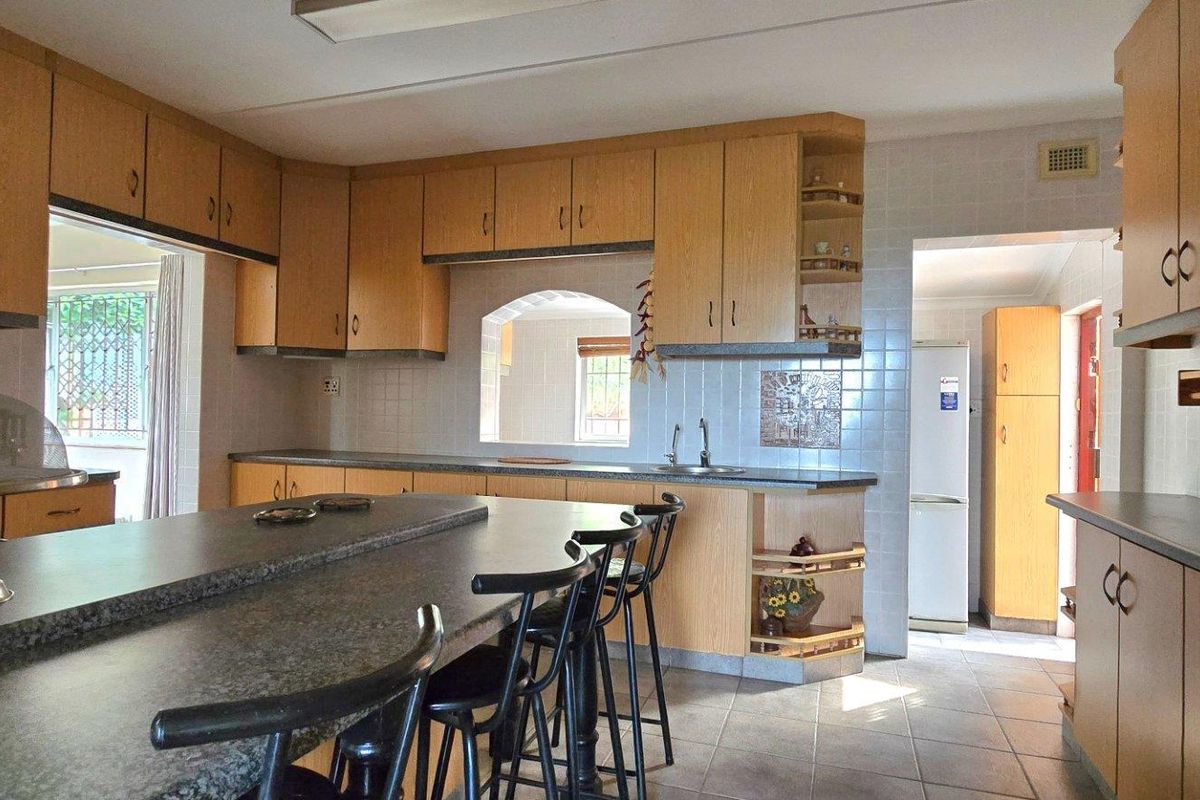 Spacious kitchen featuring light wood cabinetry, stone-look countertops, a breakfast bar, and a convenient serving hatch connecting to the adjacent living area.