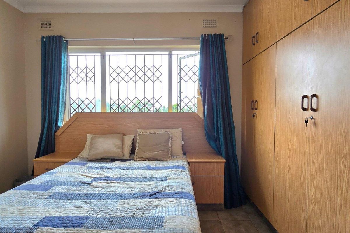 A bedroom featuring built-in wooden cupboards and a window fitted with security bars.
