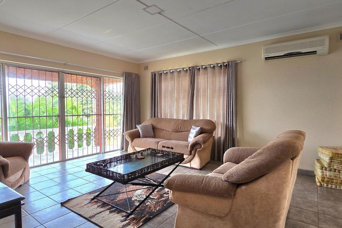 Spacious living room featuring tiled flooring, large sliding glass doors with security gates, and a wall-mounted air conditioning unit.