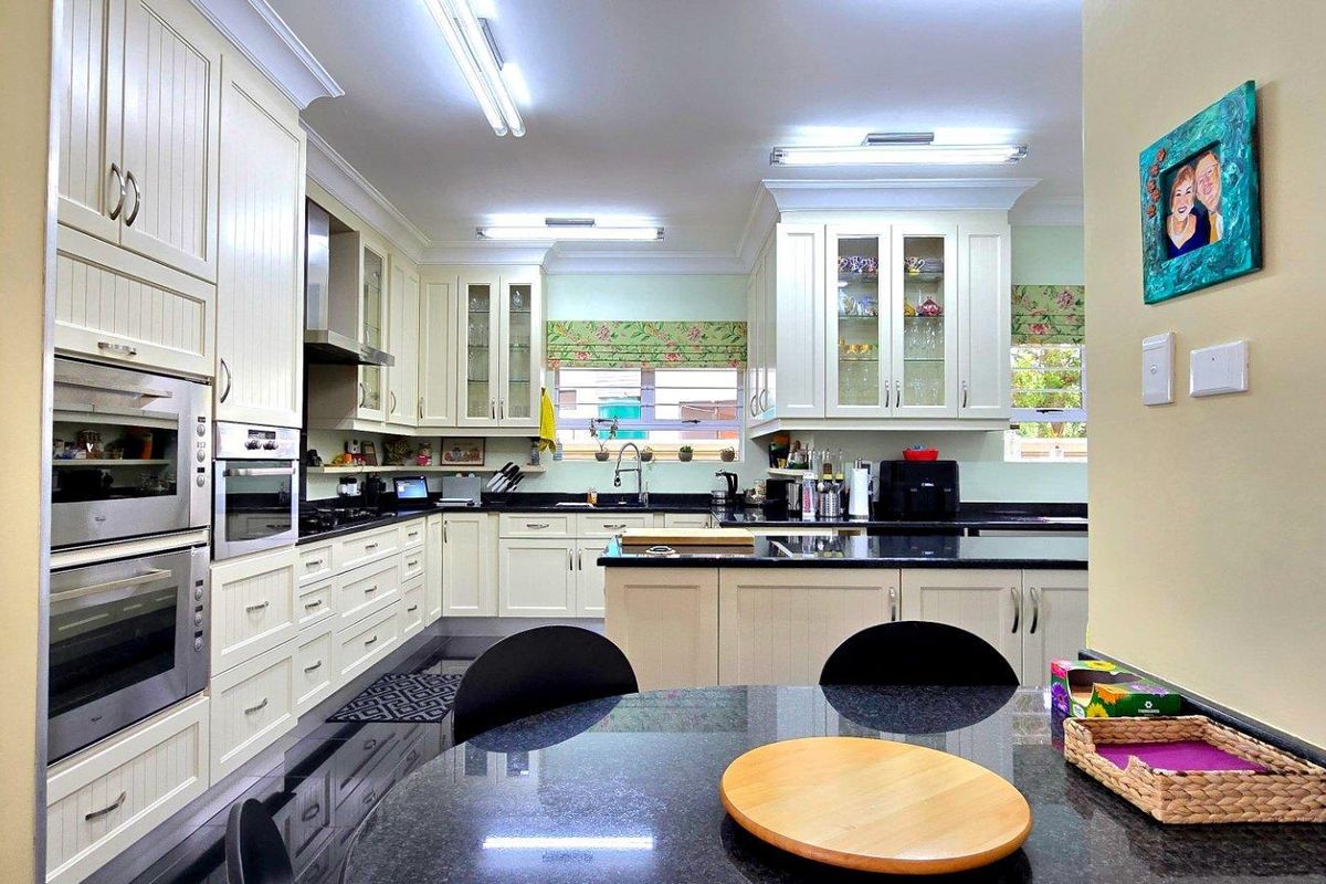 Spacious kitchen featuring cream-colored cabinetry, dark granite countertops, a central island, and integrated double wall ovens with ample storage space.