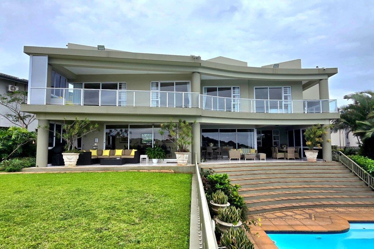 Rear view of a modern multi-story residence featuring a swimming pool, expansive lawn, covered patio areas, and large glass sliding doors.