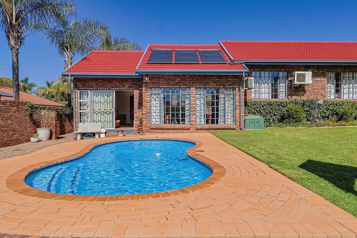 Rear view of the property featuring a brick facade, red tiled roof with solar panels, a swimming pool, and a paved patio area.