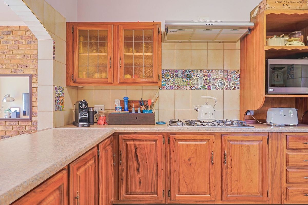 A traditional kitchen featuring warm timber cabinetry, a gas hob with extractor fan, built-in microwave housing, and decorative tiled splashbacks.