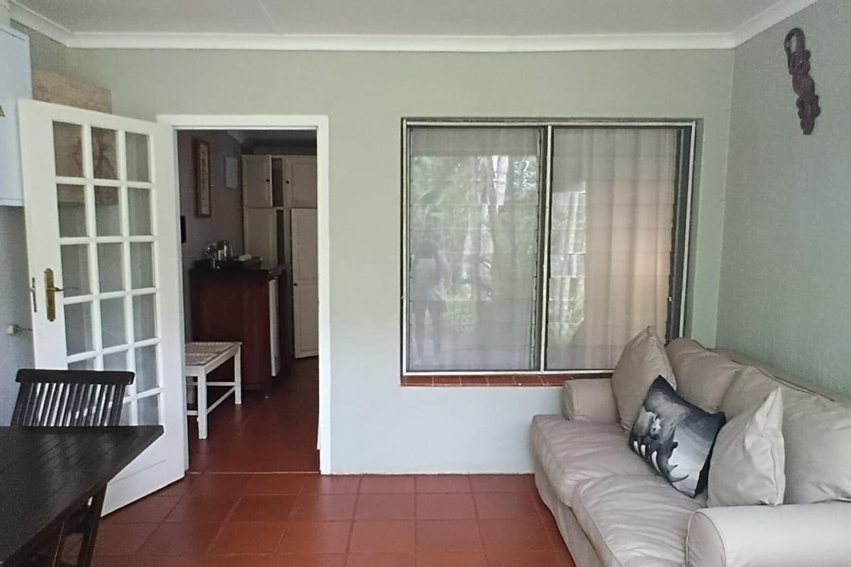 A living area featuring terracotta floor tiles, a large window, and a glass-paneled door leading to an adjacent room.