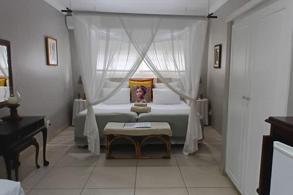 A well-maintained bedroom featuring tiled flooring, built-in wardrobe storage, and a central bed area with canopy drapery.