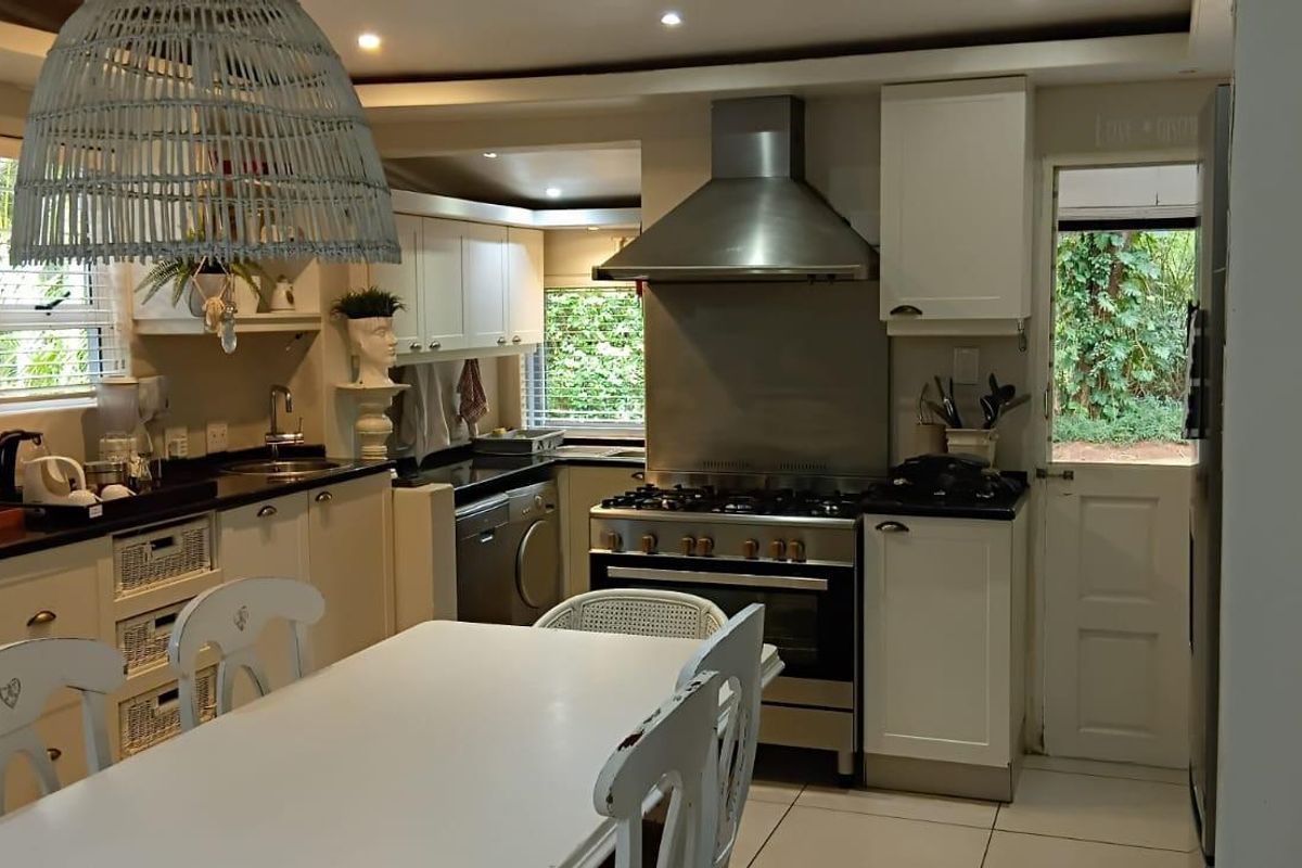 A functional kitchen featuring white cabinetry, dark countertops, a stainless steel gas range with extractor hood, and tiled flooring with direct outdoor access.