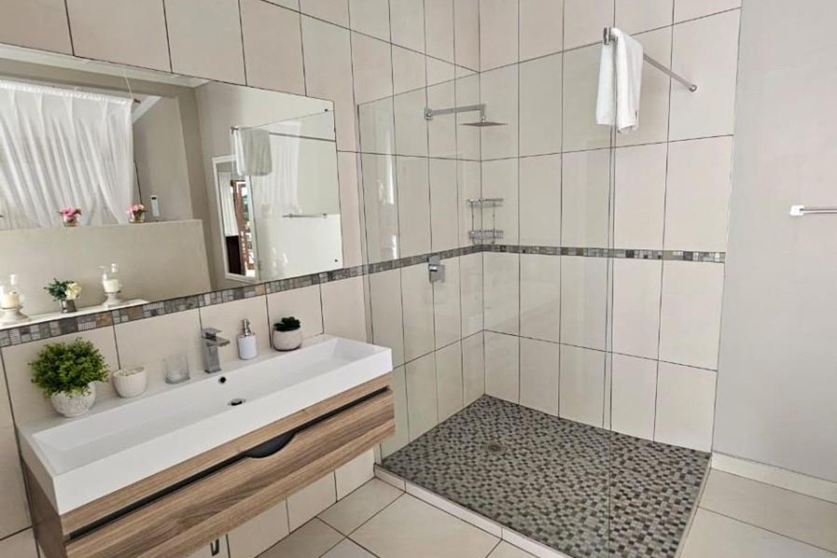 Modern bathroom featuring a floating vanity with integrated basin, large frameless glass walk-in shower with mosaic floor tiling, and neutral wall tiles.