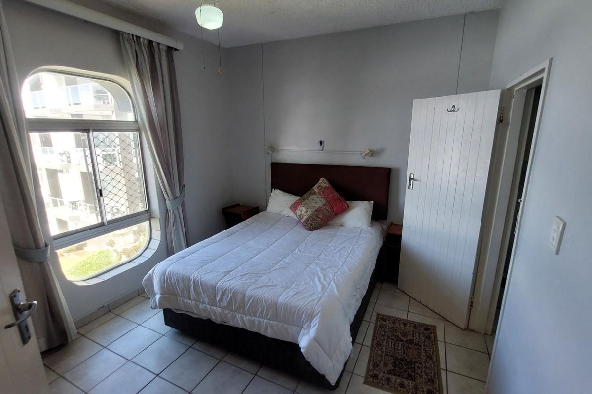 A functional bedroom featuring tiled flooring, a large arched window, and a built-in headboard with integrated wall lighting.