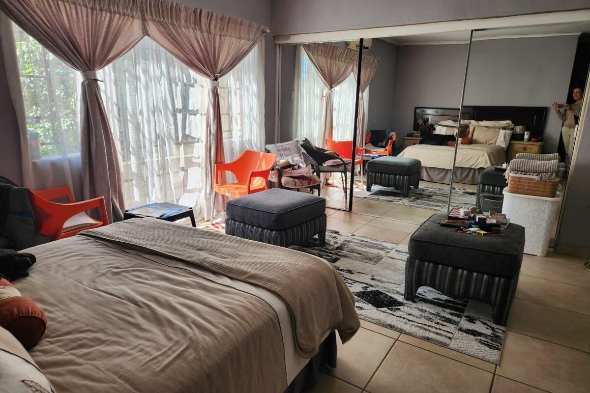 Spacious bedroom featuring large mirrored built-in cupboards, tiled flooring, and a wall-mounted air conditioning unit.