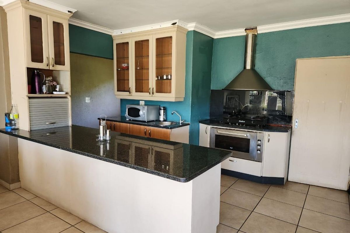 A functional kitchen featuring granite countertops, built-in oven, gas hob, stainless steel extractor fan, and ample cabinetry with glass-fronted display units.