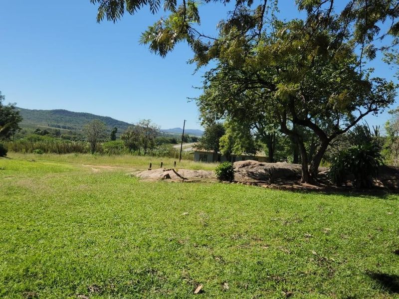 A scenic view of the expansive farm landscape featuring natural rock formations, mature trees, and open green fields under a clear sky.