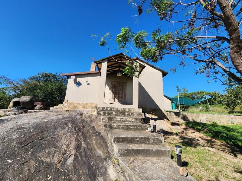 Exterior view of a rustic farm cottage featuring a covered entrance, stone foundation integration, and concrete steps leading to the front door.