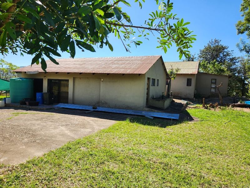 Rear view of the farm property showing the main building structure, corrugated metal roofing, concrete driveway, and an external water storage tank.