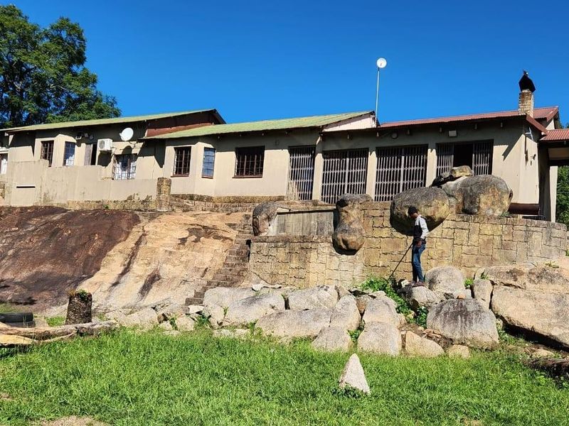 Rear view of a farm-style residence featuring a stone-built retaining wall, natural rock landscape, and a covered patio area.