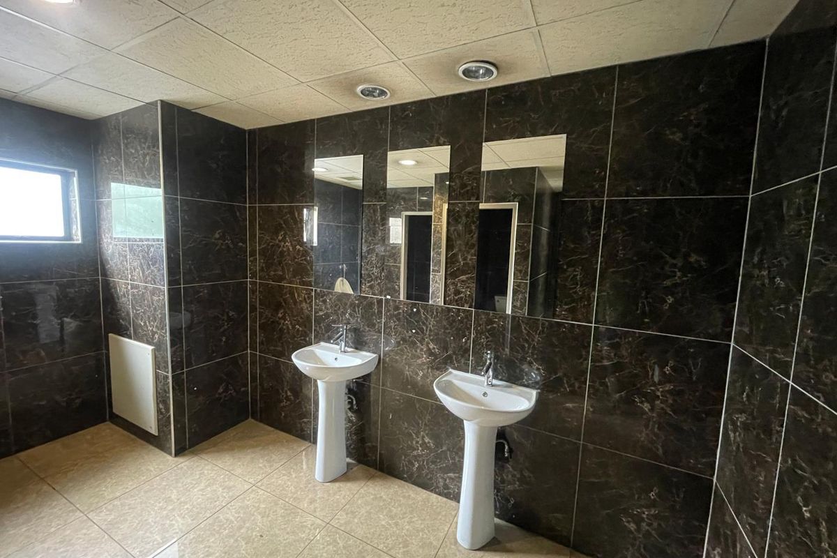 Commercial bathroom featuring dual pedestal wash basins, dark marble-effect wall tiling, and recessed ceiling lighting.